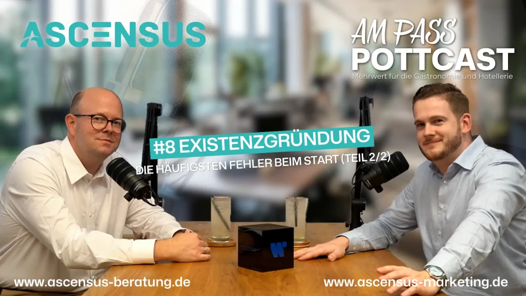 Philipp und Robert sitzen am Tisch und schauen in die Kamera bei der Podcastaufnahme